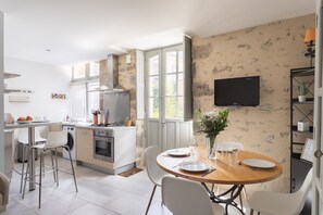A modern kitchen with a dining area, a TV mounted on the wall, and a window providing natural light.