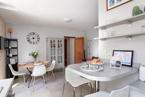 A modern kitchen with a dining table, chairs, a clock, and a refrigerator.