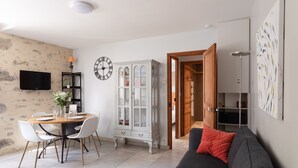 Ein Wohnzimmer mit Esstisch, Stühlen, einer Couch, einem Schrank, einem Fernseher und einer Uhr.