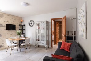 A living room with a dining table, chairs, a sofa, a cabinet, a TV, and a clock.
