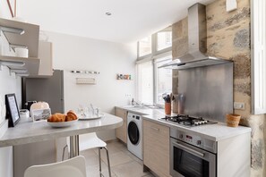 A modern kitchen with a built-in washing machine, a gas stove, and a large window with blinds.