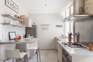 A modern kitchen with a gas stove, white cabinets, and a dining area with a white chair.