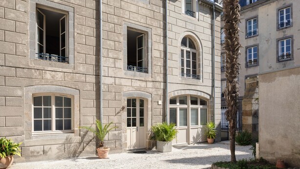 Ein Gebäude mit mehreren Fenstern, einem Kieshof und Kübelpflanzen.