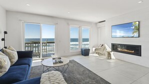 A modern living room with a large TV, a fireplace, and a view of the ocean. - Oceanfront Home w/ Panoramic Views & Private Beach (Oceanside,)