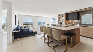 A modern kitchen with a central island, bar stools, and a large window overlooking the ocean. - Oceanfront Home w/ Panoramic Views & Private Beach (Oceanside,)