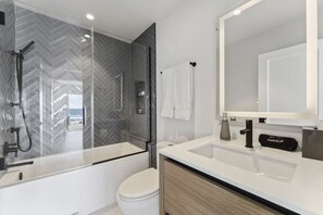 Une salle de bain moderne avec une douche à parois de verre, des toilettes blanches, un meuble-lavabo avec un miroir et une trousse de maquillage étiquetée « MAQUILLAGE » posée sur le comptoir.
