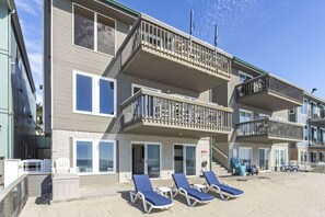 Un hôtel à plusieurs étages doté de balcons, situé en bord de mer, et proposant des chaises longues au rez-de-chaussée.