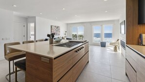 A modern kitchen with a central island, large windows, and a view of the sea. - Oceanfront Home w/ Panoramic Views & Private Beach (Oceanside,)