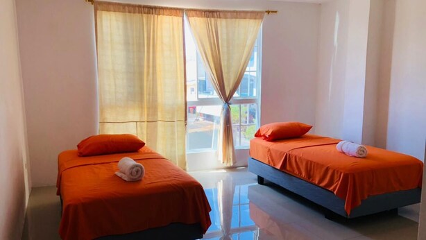 Une chambre d’hôtel avec deux lits, chacun recouvert d’une couverture orange et doté d’oreillers, une grande fenêtre avec des rideaux et un sol réfléchissant.