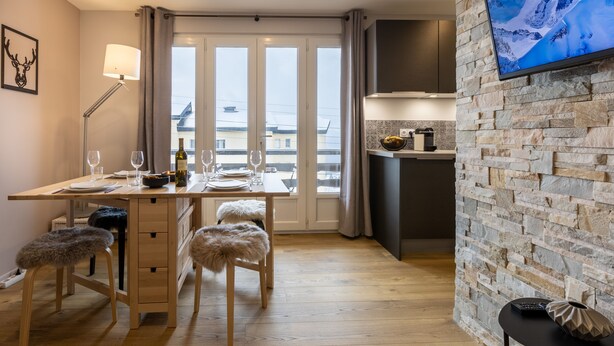 A modern kitchen with a stone wall, a dining area with a table set for two, and a TV mounted on the wall. - Orpin - superbe appartement rénové 2 personnes avec grande terrasse plein sud, belle vue (Font-Romeu)