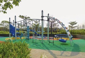 Explore the outdoor playground with a climbing wall, slides, and swings set amidst lush surroundings.