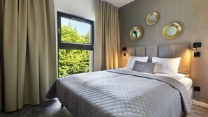 A modern hotel room with a large bed, a view of greenery through a window, and decorative wall mirrors. - Elite Apartments Rezydencja Wintera (Gdansk)