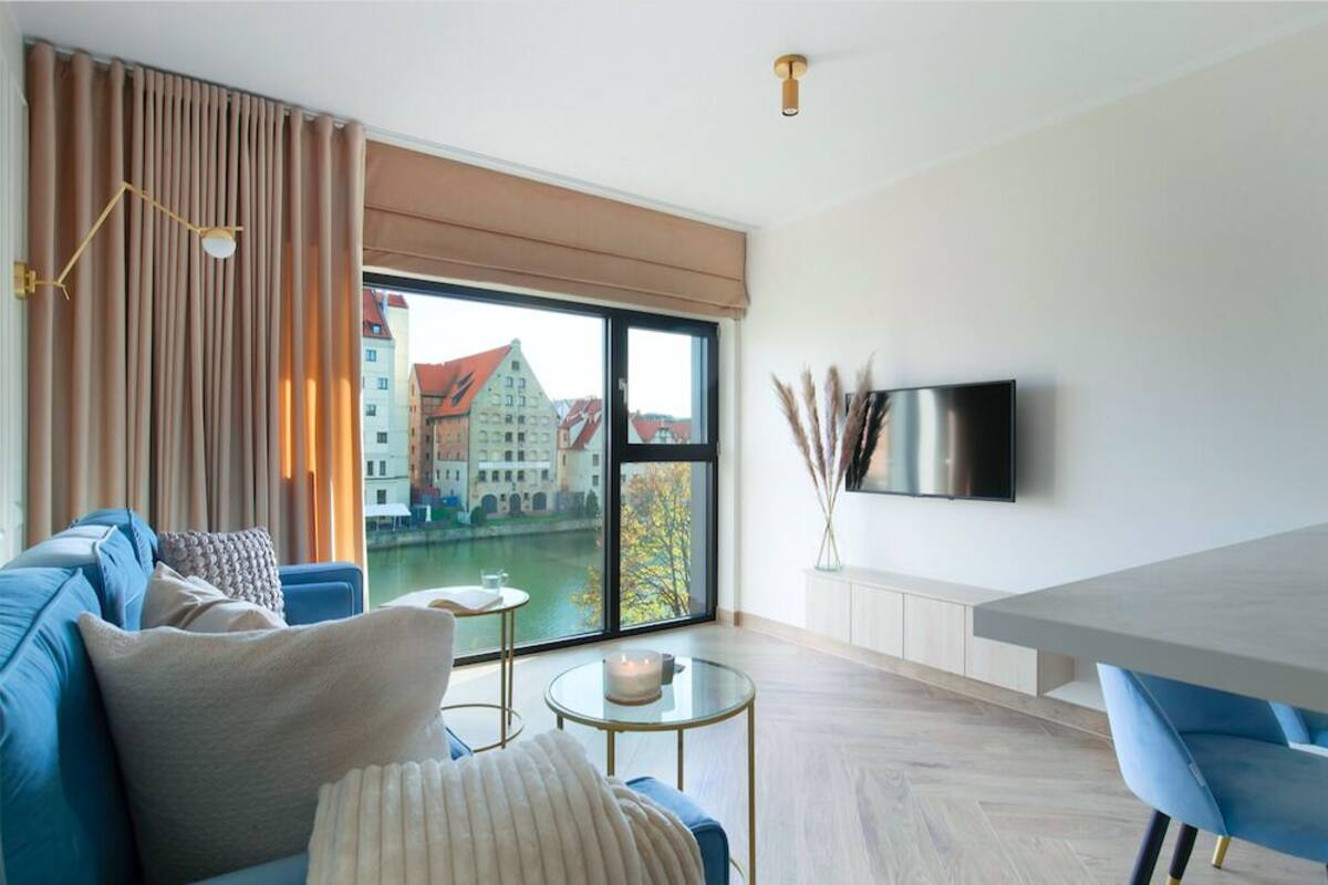 A modern living room with a large window, a sofa, a coffee table, and a flat-screen TV.