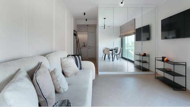 A modern living room with a sofa, a dining area with a table and chairs, and a black metal shelf with candles. - Elite Apartments Rezydencja Wintera (Gdansk)
