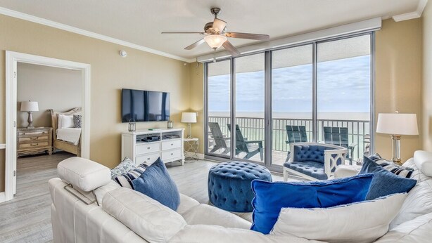 A spacious living room with a white sofa set, a ceiling fan, and a large sliding glass door leading to a balcony with outdoor furniture. - Beauty on the Beach - Emerald Dolphin 3B w/Amazing Gulf Views. (Pensacola Beach)