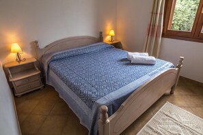 A bedroom with a bed, two bedside tables with lamps, a window with curtains, and a rug on the floor. - Flat with Pool in Badus Resort (Badesi)