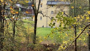 Puiden ympäröimä rakennus, jonka ympärillä on syksyisestä lehdistöstä peittynyt nurmialue ja kirkas taivas.