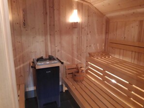 A sauna room with wooden benches and a bench heater. - Exclusive family suite in the Erzgebirge Nature Park (Breitenbrunn/Erzgebirge)