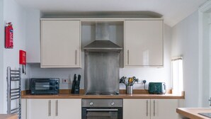 A compact kitchen with a microwave, oven, and stainless steel range hood. There is a window providing natural light and a fire extinguisher mounted on the wall. - Hawthorn- Great 2 bed home in Ashington, Northumberland (Ashington)