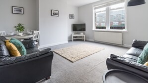 A modern living room with a dining area, featuring a sofa, a coffee table, a TV, and framed pictures on the wall. - Hawthorn- Great 2 bed home in Ashington, Northumberland (Ashington)