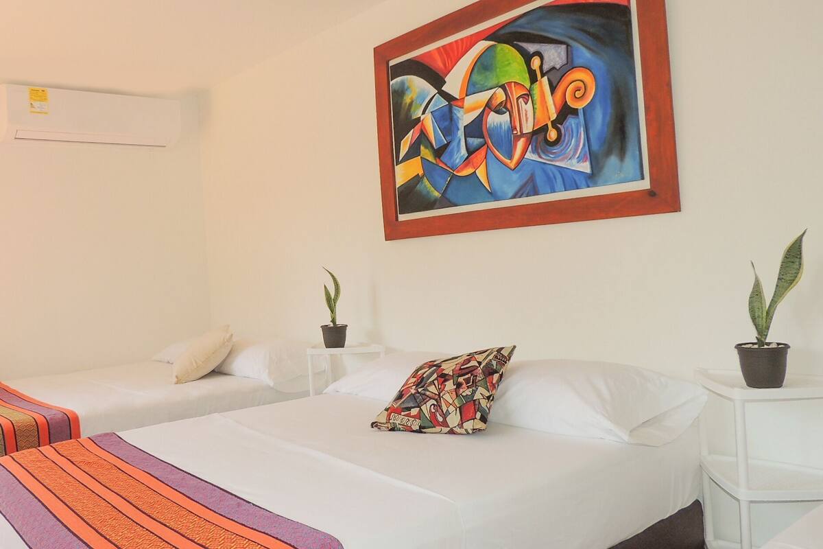 Ein Hotelzimmer mit zwei Betten, einem Bild an der Wand und zwei Zimmerpflanzen.