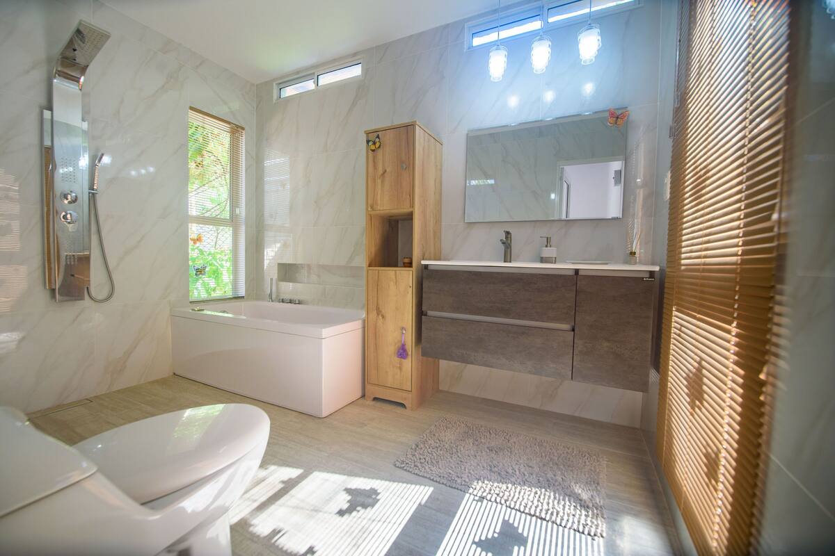 Ein modernes Badezimmer mit Badewanne, Toilette, Waschtisch inklusive Spiegel und einem Holzschrank.