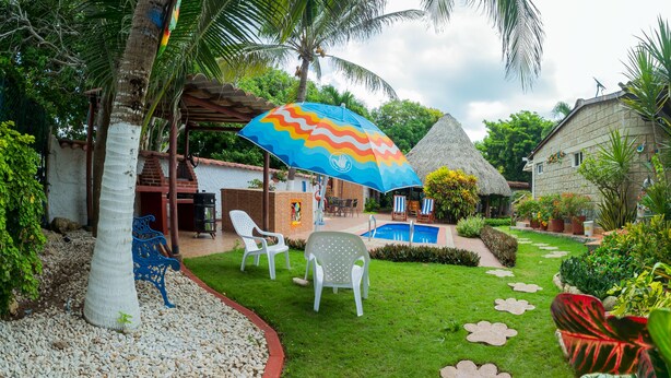 A tropical garden with a pool, white chairs, and a colorful umbrella. - Portoazul Casa de Playa (Puerto Colombia)