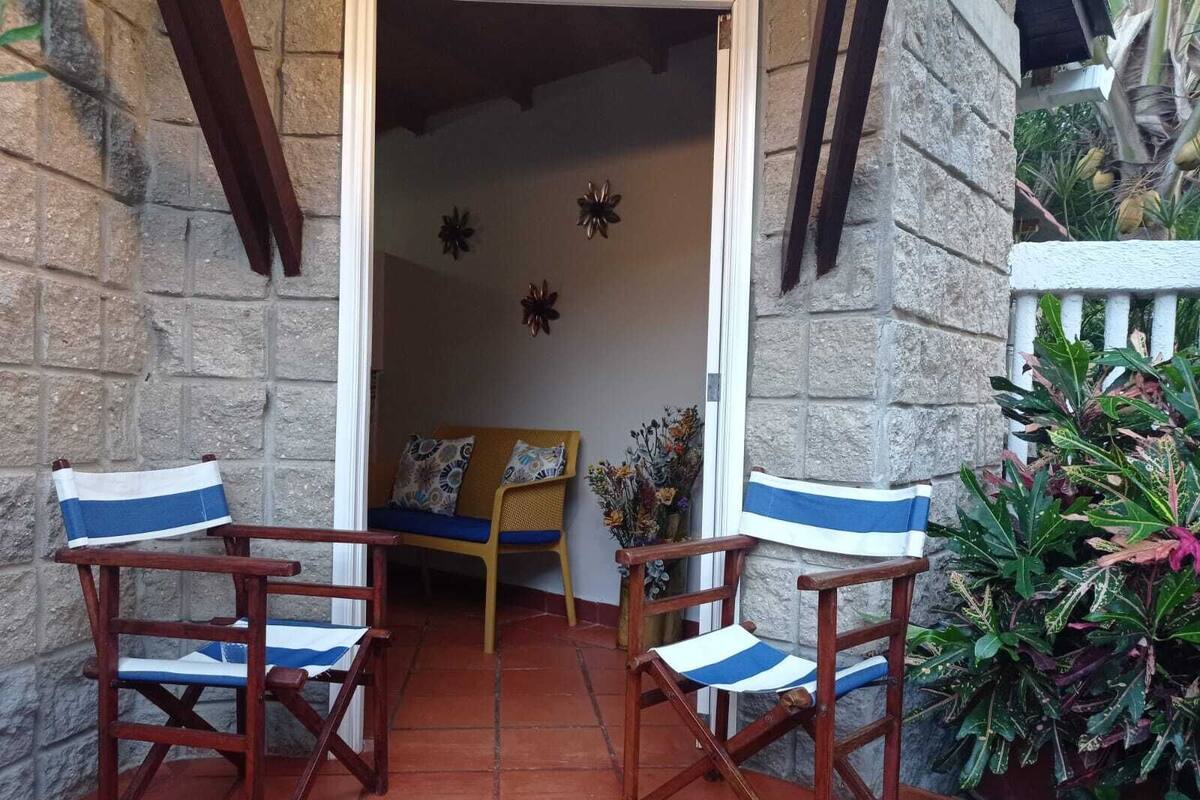 Eine Terrasse mit zwei Holzstühlen, einem kleinen Tisch, einer Steinmauer und einer Tür.