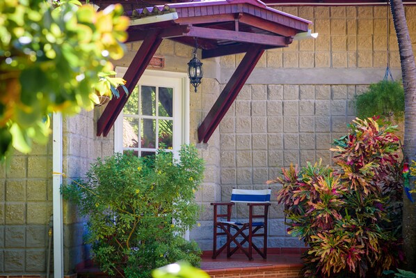 A covered patio with a wooden chair and a table, surrounded by plants and a stone wall. - Portoazul Casa de Playa (Puerto Colombia)