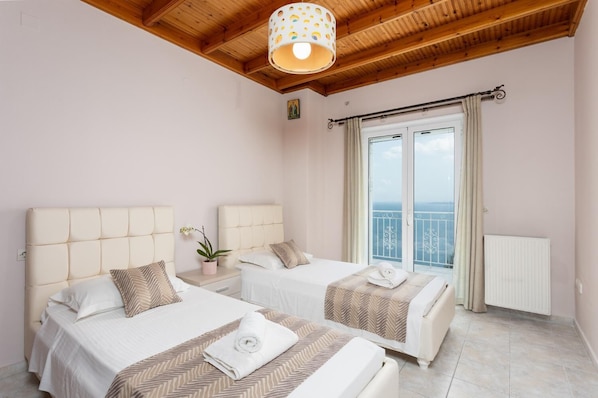 Une chambre avec deux lits, un ventilateur de plafond, une plante en pot et une vue sur la mer, visible par une porte coulissante.