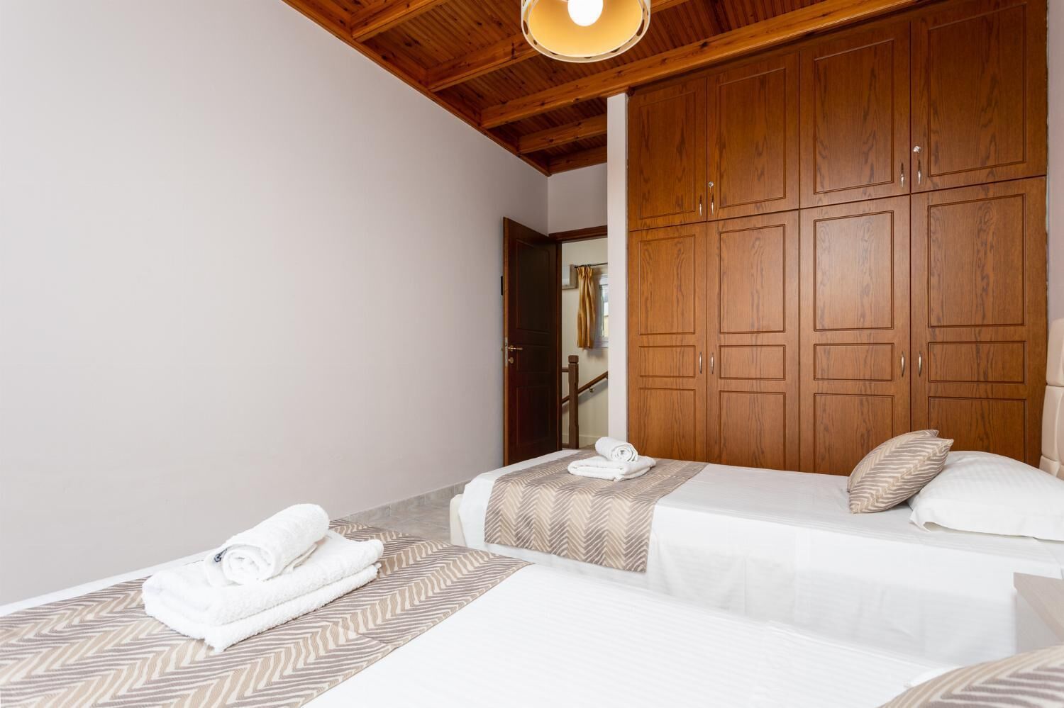 A hotel room with two beds, wooden wardrobe, and a ceiling light.
