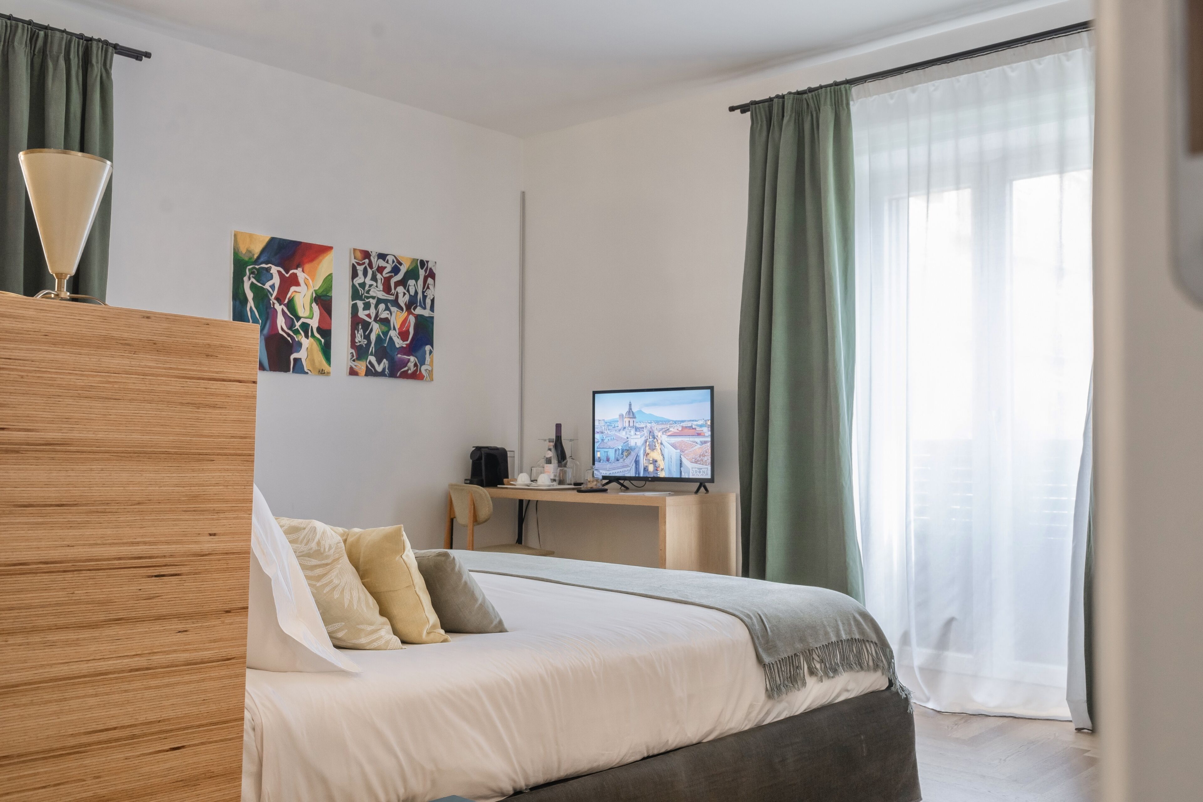 A modern hotel room with a large bed, a desk with a computer, and artwork on the wall.