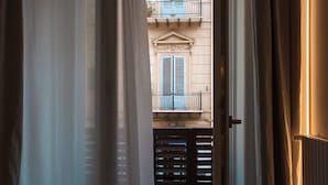 A view through a doorway with a building facade, featuring a balcony with blue shutters and a door with a metal grille. - Archè Design Rooms and Suites (Palermo)