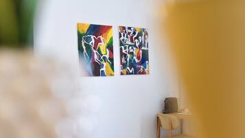 Two abstract paintings on a white wall, a wooden chair, and a small table with a cup.
