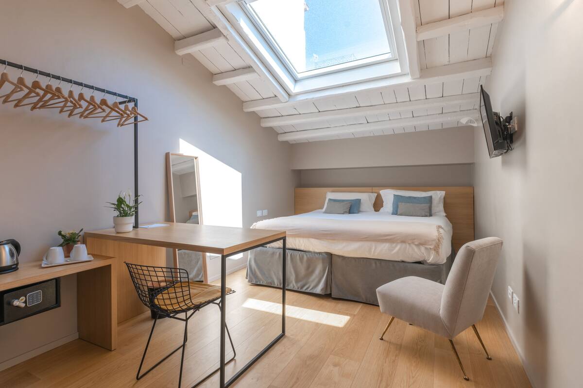 A modern bedroom with a skylight, a bed, a desk, and a chair.
