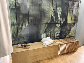 Una panca di legno con un vassoio di candele e piccole piante, un asciugamano bianco arrotolato e un muro con linee verticali che riflettono la luce.