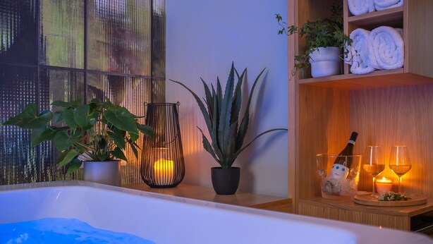 A spa area with a bathtub, potted plants, a shelf with towels, and a bottle of champagne. - Archè Design Rooms and Suites (Palermo)
