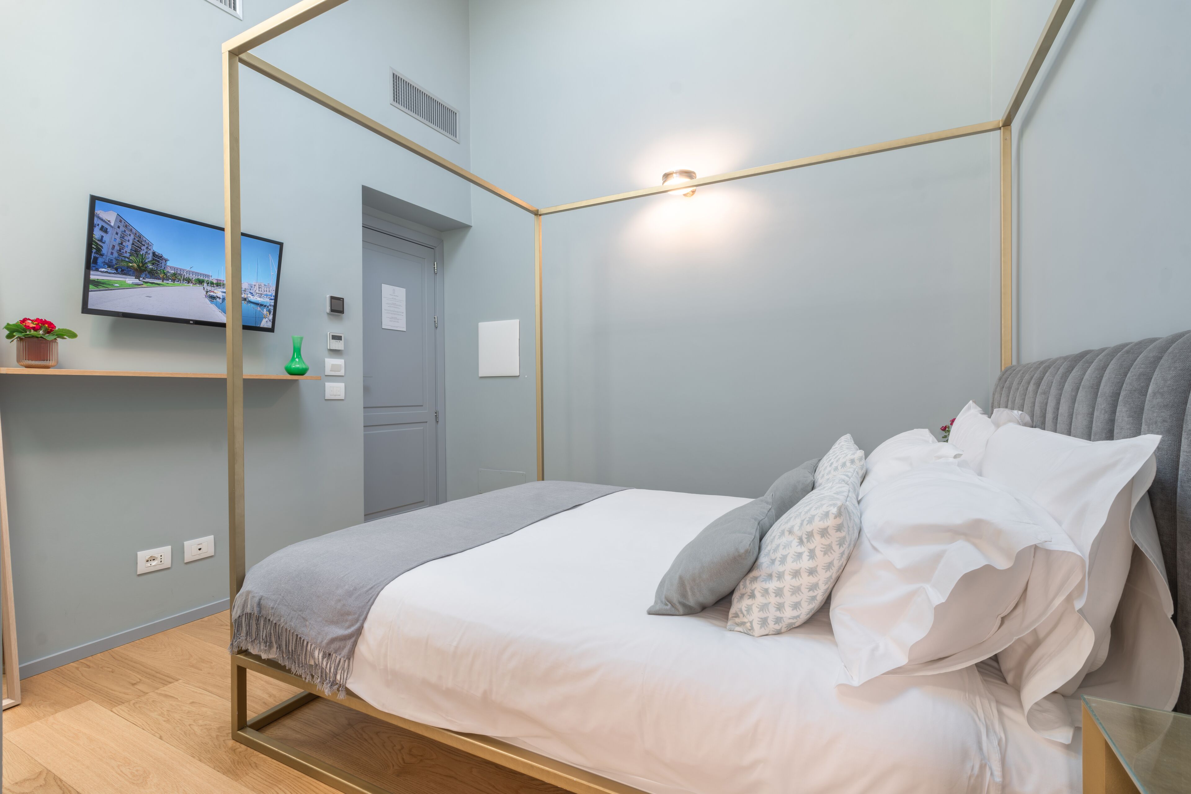 A modern bedroom with a four-poster bed, a flat-screen TV on a shelf, and a small potted plant.