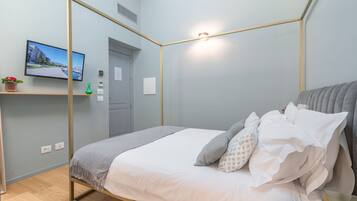 A modern bedroom with a four-poster bed, a flat-screen TV on a shelf, and a small potted plant.