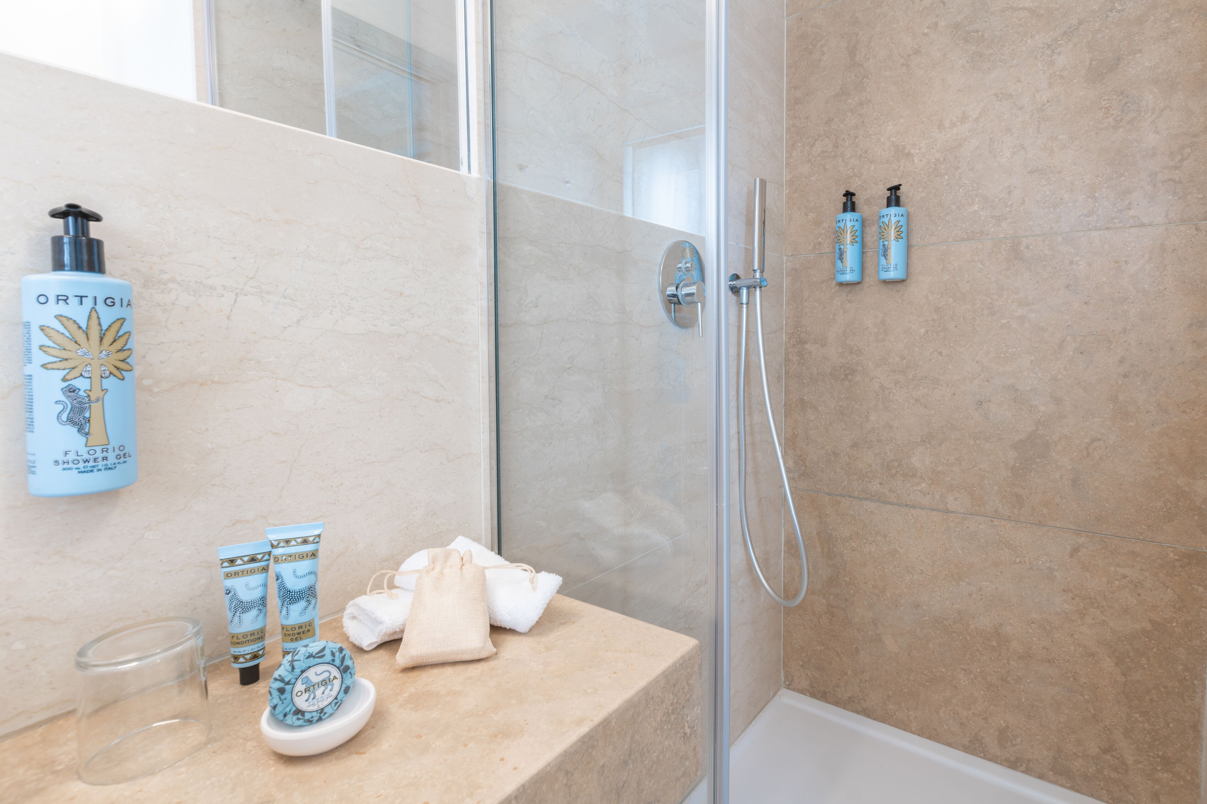 A bathroom with a shower, a sink, and toiletries including a shower gel bottle, a soap bar, and a towel.