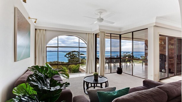 A spacious living room with a large window offering a view of the sea and mountains. - The Bay- Stunning water views (Nelson Bay)