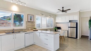 A modern kitchen with white cabinetry, a stainless steel refrigerator, and a dining area with a table and chairs. - The Bay- Stunning water views (Nelson Bay)
