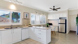 A modern kitchen with white cabinetry, a stainless steel refrigerator, and a dining area with a table and chairs. - The Bay- Stunning water views (Nelson Bay)