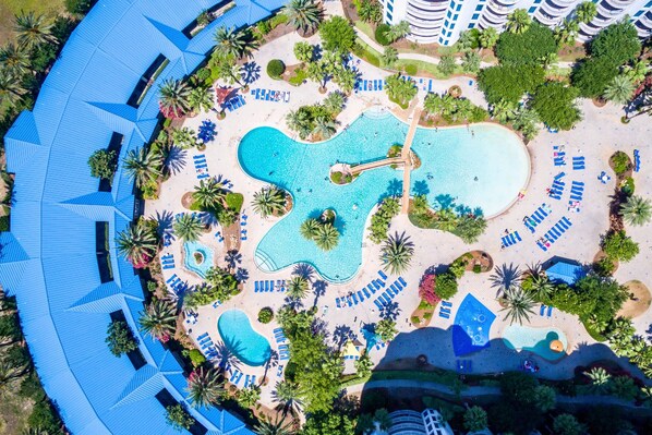 An aerial view of a resort with multiple swimming pools, sun loungers, and palm trees.