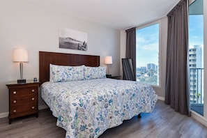Habitación de hotel con una cama grande, dos mesitas de noche, una lámpara de noche, vista a la ciudad y un cuadro en la pared.