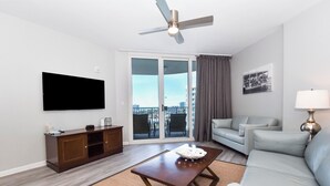 A modern living room with a flat-screen TV, a ceiling fan, a sofa, a coffee table, and a sliding glass door to the outside.