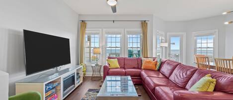 A living room with a flat-screen TV, a red leather sofa, a glass coffee table, and a ceiling fan.