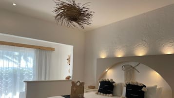 Een moderne slaapkamer met een groot bed, een bankje, een decoratieve plafondlamp en uitzicht op palmbomen door het raam.