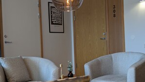 A room with two grey armchairs, a round wooden table, a hanging light fixture, and a door labeled '308'. - Hotell Bro (Kristinehamn)