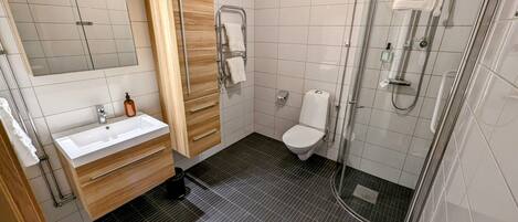 Un baño moderno con lavamanos, inodoro y ducha con mampara de vidrio.
